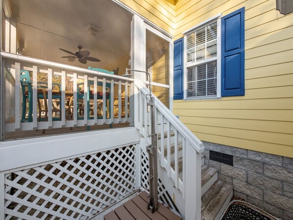 A wooden staircase leading to a porch with a white railing and a blue window shutter.