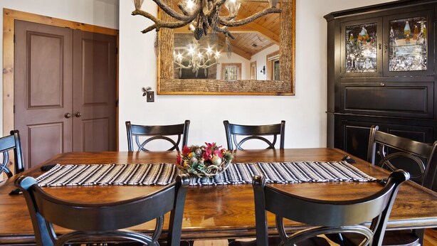 A dining area with a wooden table, black chairs, a chandelier, and a large mirror on the wall. - Grand Oaks B6- Mountain Condo, Gated Resort, Indoor/Outdoor Pools & Hot Tub (Boone)