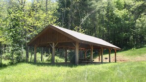 A wooden pavilion with a sloped roof, surrounded by a grassy area and dense forest. - Grand Oaks B6- Mountain Condo, Gated Resort, Indoor/Outdoor Pools & Hot Tub (Boone)