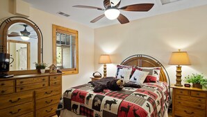 A bedroom with a wooden headboard, a quilted bedspread, two bedside lamps, a ceiling fan, a wooden dresser, and a mirror. - Grand Oaks B6- Mountain Condo, Gated Resort, Indoor/Outdoor Pools & Hot Tub (Boone)