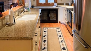 A modern kitchen with a large island, stainless steel appliances, and a rustic brick wall. - Grand Oaks B6- Mountain Condo, Gated Resort, Indoor/Outdoor Pools & Hot Tub (Boone)