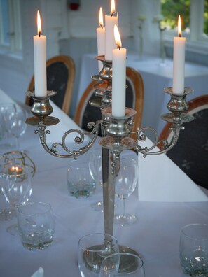Une table dressée avec des bougies blanches sur des chandeliers en métal ouvragé, entourée de verres à vin vides.