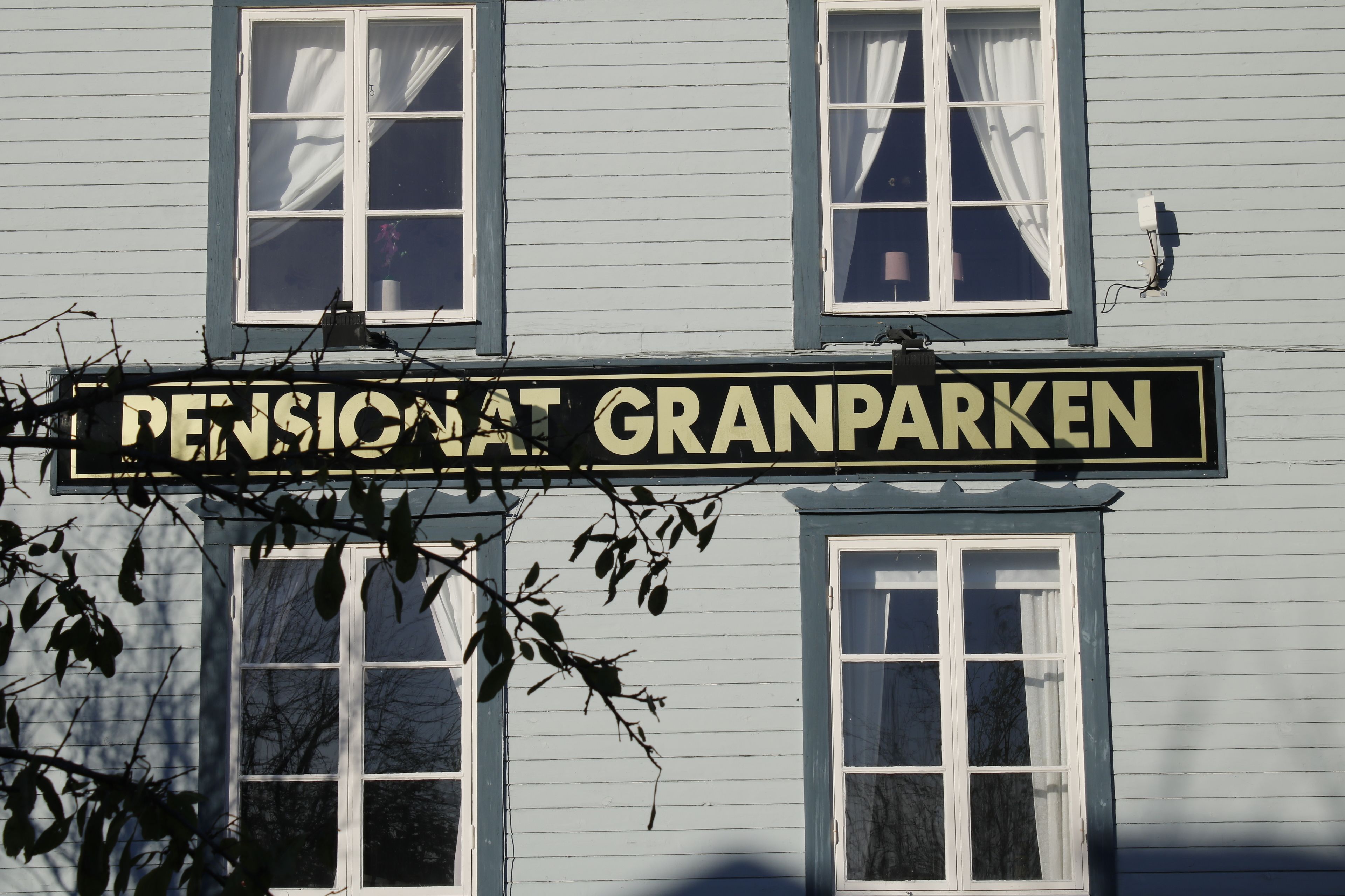 A building with a sign reading "Pensionat Granparken" and multiple windows with curtains.