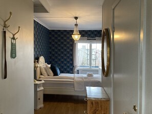 Une chambre à coucher comprenant un lit, une table de chevet, une commode, un lustre et une fenêtre avec des rideaux.