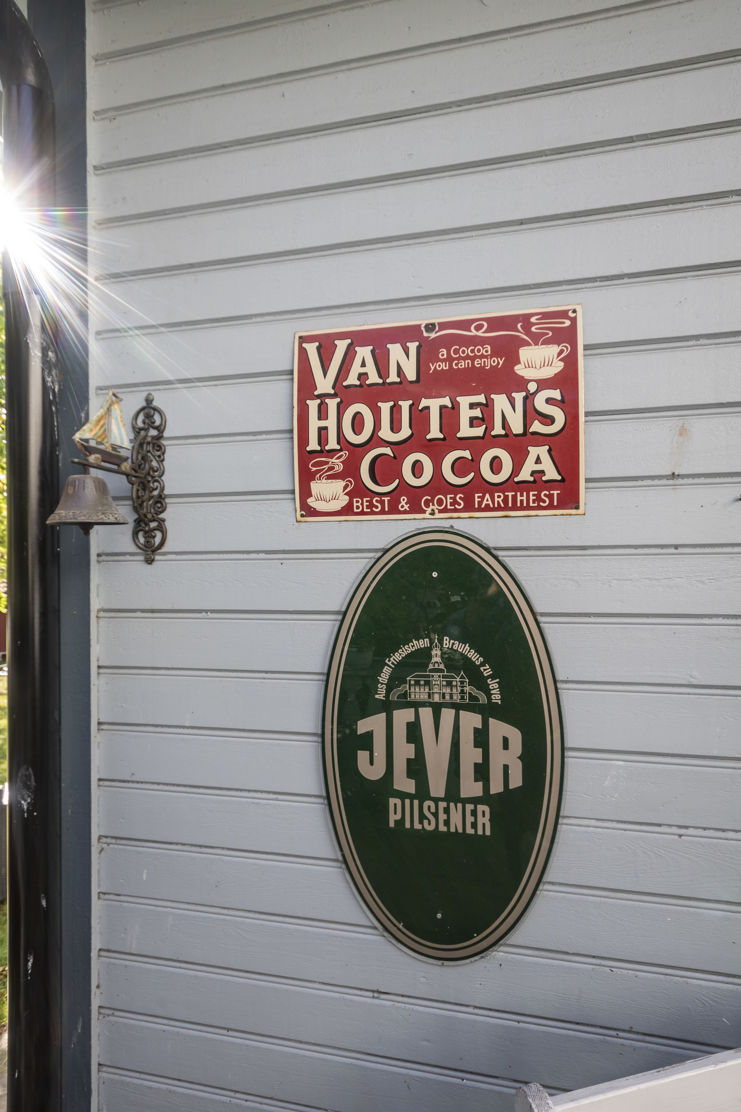 A sign for Van Houtens Cocoa and a beer sign for Jever Pilsener on a white wooden wall.