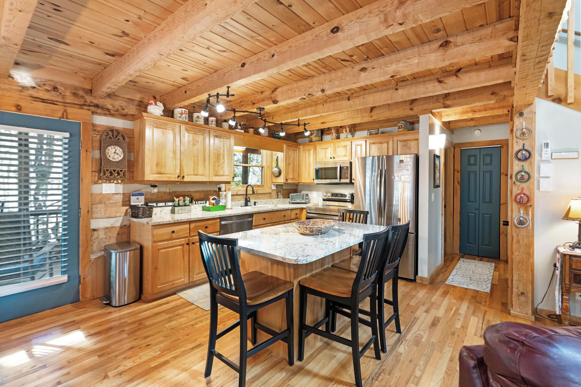 A spacious kitchen with wooden cabinets, a central island with chairs, stainless steel appliances, and a window with blinds.