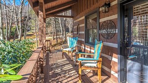 A wooden deck with Adirondack chairs, a covered porch, and a door with a tree decal. - A Portofino Cabin: Mountain Log Cabin, Hot Tub, Pet Friendly, Wood Fireplace (Seven Devils)