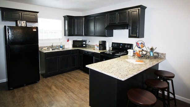 A modern kitchen with dark cabinetry, a black refrigerator, a microwave, a stove, and a granite countertop with bar stools. - Awesome Location 2 Bedroom 2.5 Bath / 511B (Lake Charles)
