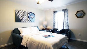 A hotel room with a bed, a chair, a lamp, and artwork on the wall. - Awesome Location 2 Bedroom 2.5 Bath / 511B (Lake Charles)