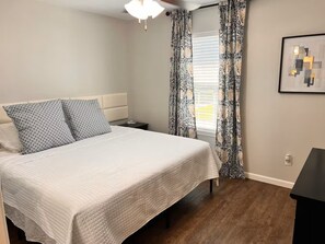 Un dormitorio con cama, mesita de noche y ventana con cortinas.