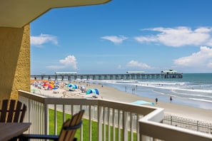 A beach view with a pier extending into the water, a fenced area with umbrellas, and a balcony with chairs. - Stay @ Peaches & Cream on Folly Beach (Folly Beach)