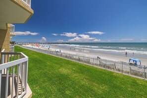 Vista a la playa con una zona verde, una valla y un muelle al fondo.