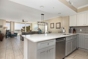 A modern kitchen with white cabinets, a large island, and a dining area with a view. - Stay @ Peaches & Cream on Folly Beach (Folly Beach)