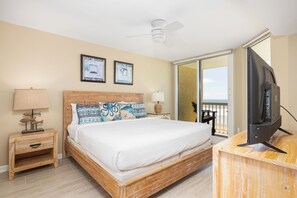 A bedroom with a bed, a nightstand, a lamp, a television, and a balcony with a view. - Stay @ Peaches & Cream on Folly Beach (Folly Beach)