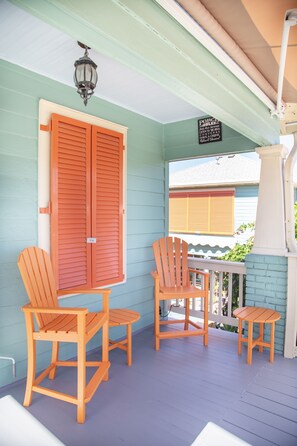 Une véranda avec deux chaises en bois et une petite table, une porte en bois et une lanterne suspendue.