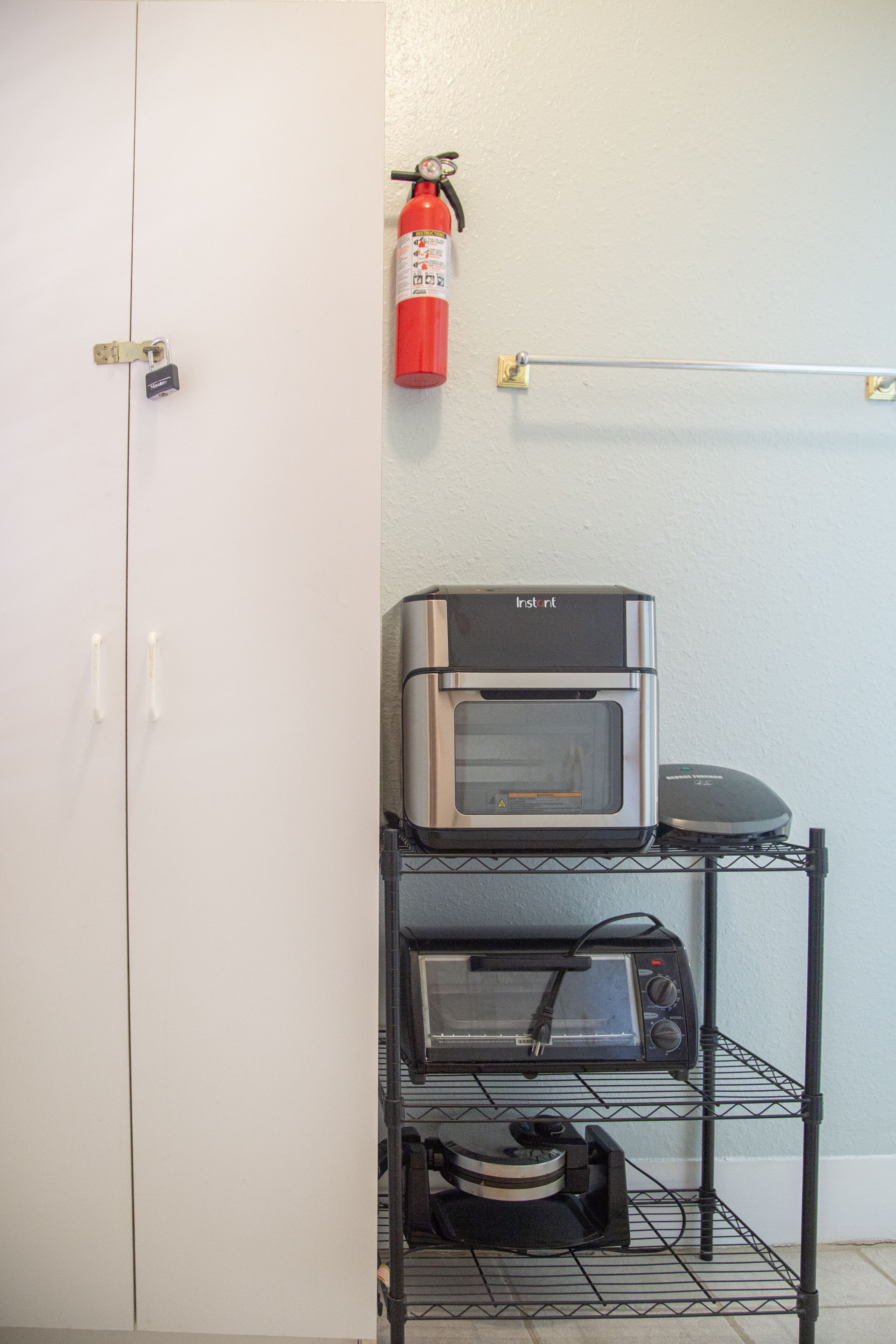 A kitchenette with a microwave, toaster oven, and a coffee maker on a wire shelf.