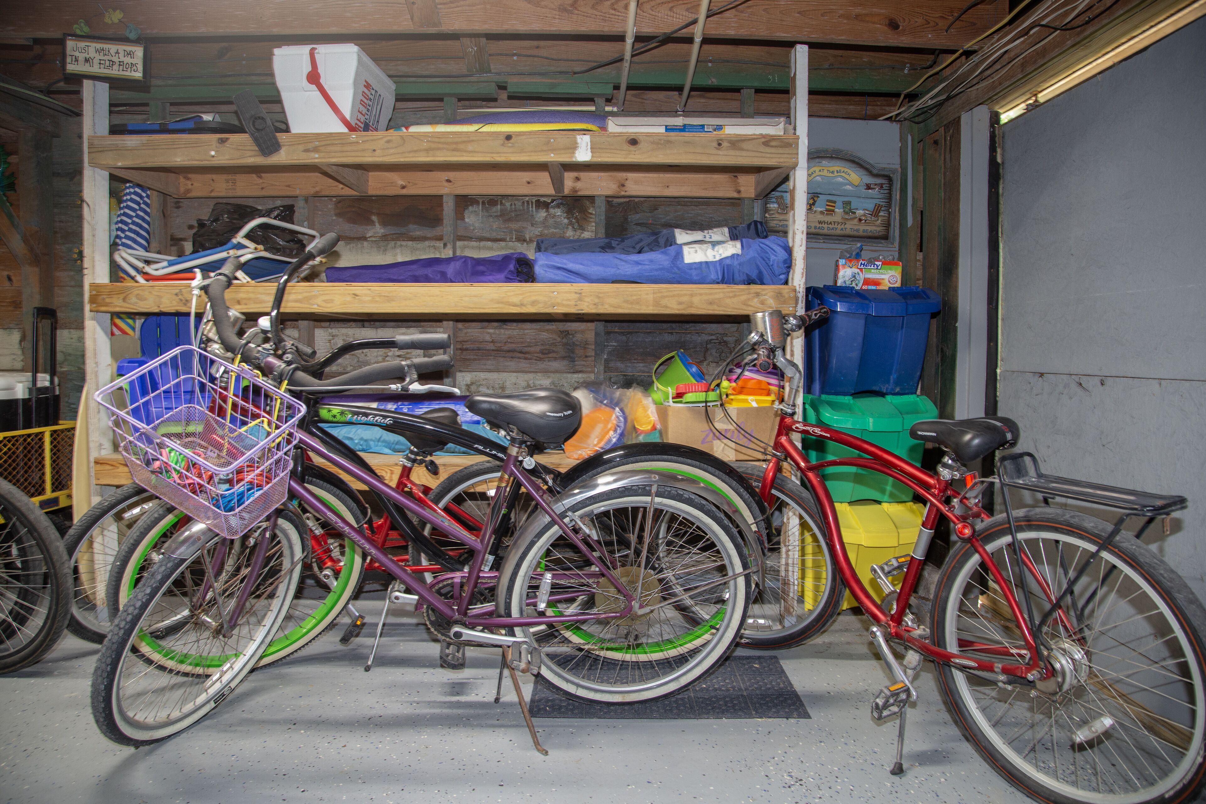 Des vélos sont garés dans un garage, et une étagère en bois située au-dessus contient divers objets.