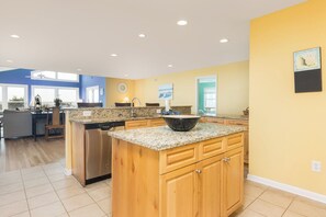 A modern kitchen with granite countertops, wooden cabinets, and a large island. - Stay @ Fun in the Sun! (Folly Beach)