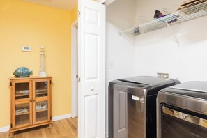 A laundry room with two dryers, a wooden cabinet with glass doors, and a thermostat on the wall. - Stay @ Fun in the Sun! (Folly Beach)
