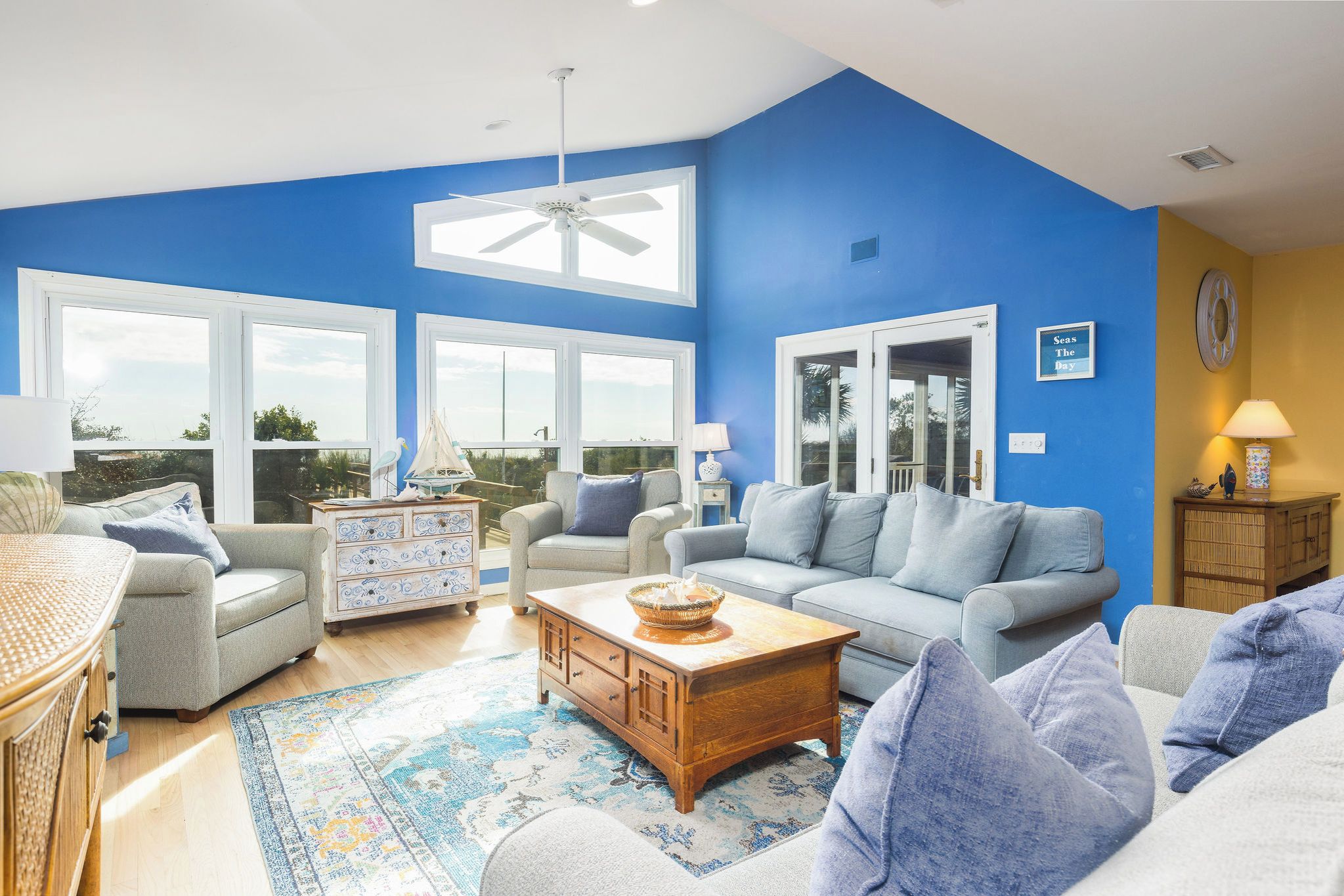 A spacious living room with a blue accent wall, large windows, and a ceiling fan.