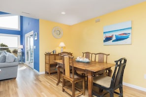 A dining area with a wooden table and chairs, a clock on the wall, and a painting of boats.
