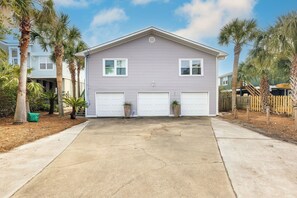 A two-story house with a garage, surrounded by palm trees and a wooden fence. - Stay @ Fun in the Sun! (Folly Beach)