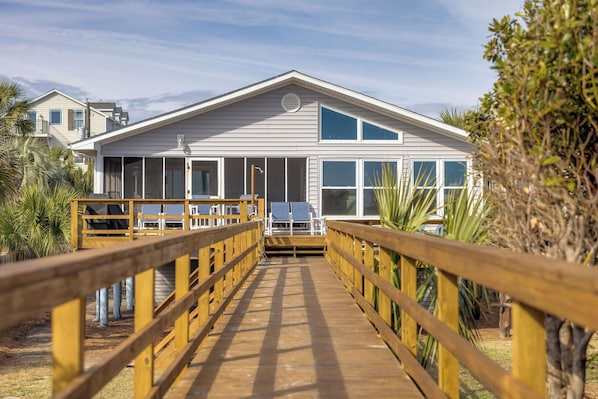 A beachfront house with a wooden deck leading to a covered patio area.