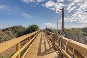 A wooden boardwalk leading to a beach, with a metal structure on the right and a wooden fence on the left. - Stay @ Fun in the Sun! (Folly Beach)