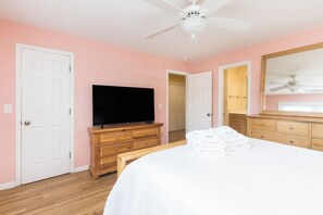 A bedroom with a bed, a television, a dresser, a mirror, and a ceiling fan. - Stay @ Fun in the Sun! (Folly Beach)