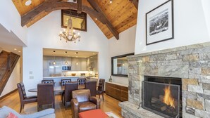 A spacious living area with a stone fireplace, wooden ceiling beams, and a modern kitchen in the background. - Courcheval D | Luxury Mountain Townhome with Views, Fireplaces & Ski Access (Mountain Village)