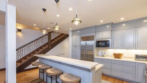 A modern kitchen with a central island, bar stools, a stainless steel refrigerator, and a microwave. - Courcheval D | Luxury Mountain Townhome with Views, Fireplaces & Ski Access (Mountain Village)