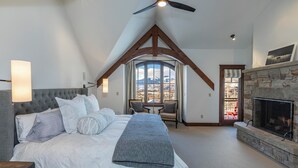 A bedroom with a large bed, a fireplace, a ceiling fan, and a view of mountains through a window. - Courcheval D | Luxury Mountain Townhome with Views, Fireplaces & Ski Access (Mountain Village)