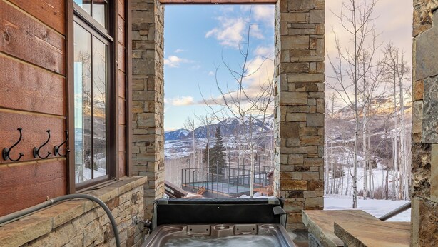 A hot tub with a view of snow-covered mountains and bare trees through a stone-framed window. - Courcheval D | Luxury Mountain Townhome with Views, Fireplaces & Ski Access (Mountain Village)
