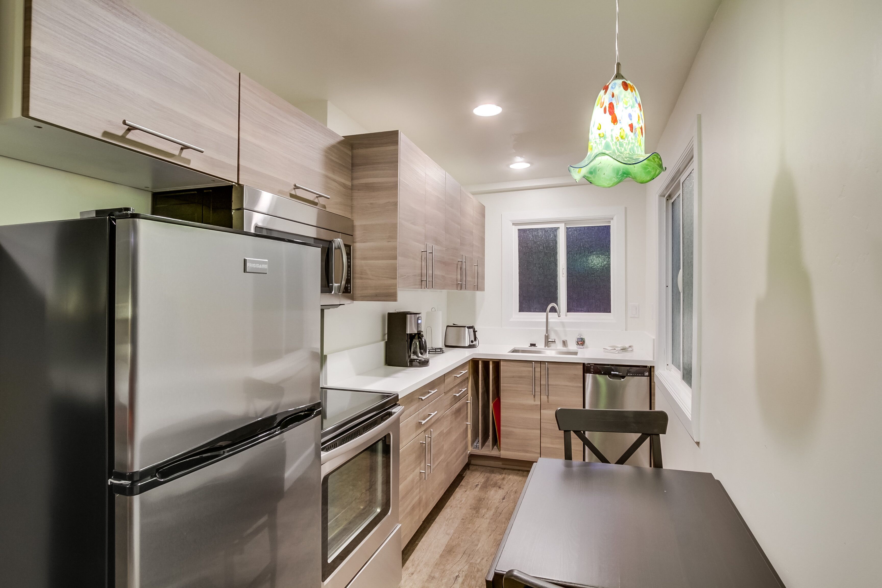 Una cocina moderna con electrodomésticos de acero inoxidable, armarios de madera, una mesa de comedor y una lámpara colgante de colores.
