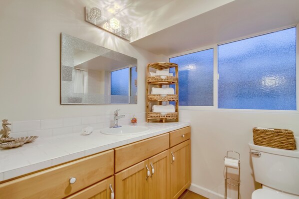 A bathroom with a white sink, wooden cabinets, a mirror, and a window with frosted glass.