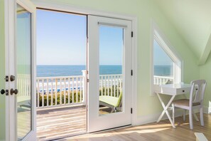 A room with a white desk, a chair, and a view of the ocean through a sliding glass door.