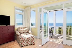 A room with a bed, a TV, a balcony with a view of the sea, and a wooden floor.
