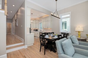 A modern kitchen with white cabinets, a dining area with a table and chairs, and a staircase leading to another level. - Stay @ Pavilion Paradise on Isle of Palms (Isle of Palms)