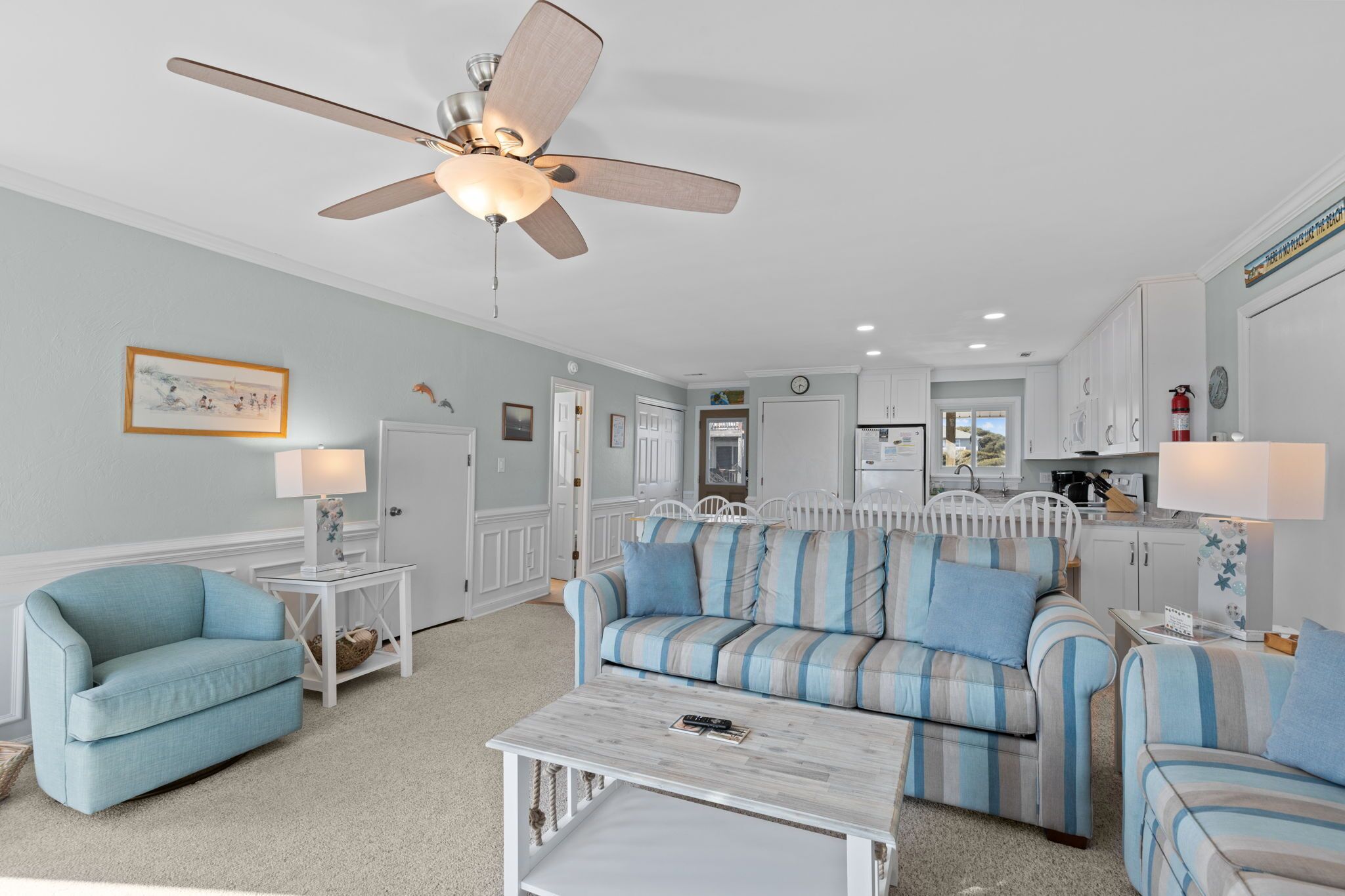 A spacious living room with a ceiling fan, a light-colored sofa, a striped armchair, and a coffee table.
