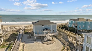 A beachfront property with a beach house, a wooden boardwalk, and a sandy beach.