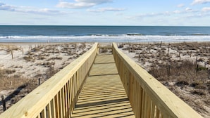 A wooden boardwalk leading to a beach with a clear view of the ocean.