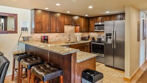 A kitchen with wooden cabinets, granite countertops, stainless steel appliances, and a bar stool area. - ✨ Newly Remodeled Sleeps 8 Pool, Hot Tubs,Fireplace, Private Deck (Steamboat Springs)