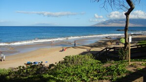 Ein Strand mit blauem Himmel, ruhiger See und einem entfernten Berg.