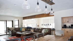 A spacious living room with a large wooden dining table, a brown leather sofa, and a red patterned rug. - Luxury home less than a mile from Deer Valley with free shuttle to and from DV (Park City)