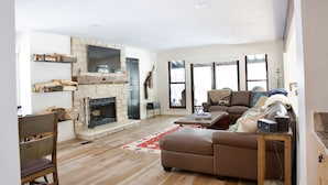 A cozy living room with a stone fireplace, a sofa, a coffee table, and a wooden floor. - Luxury home less than a mile from Deer Valley with free shuttle to and from DV (Park City)