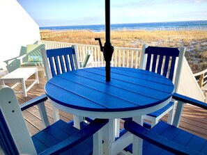 Un tavolo rotondo con sedie blu e bianche su un pontile di legno con vista sull'oceano.