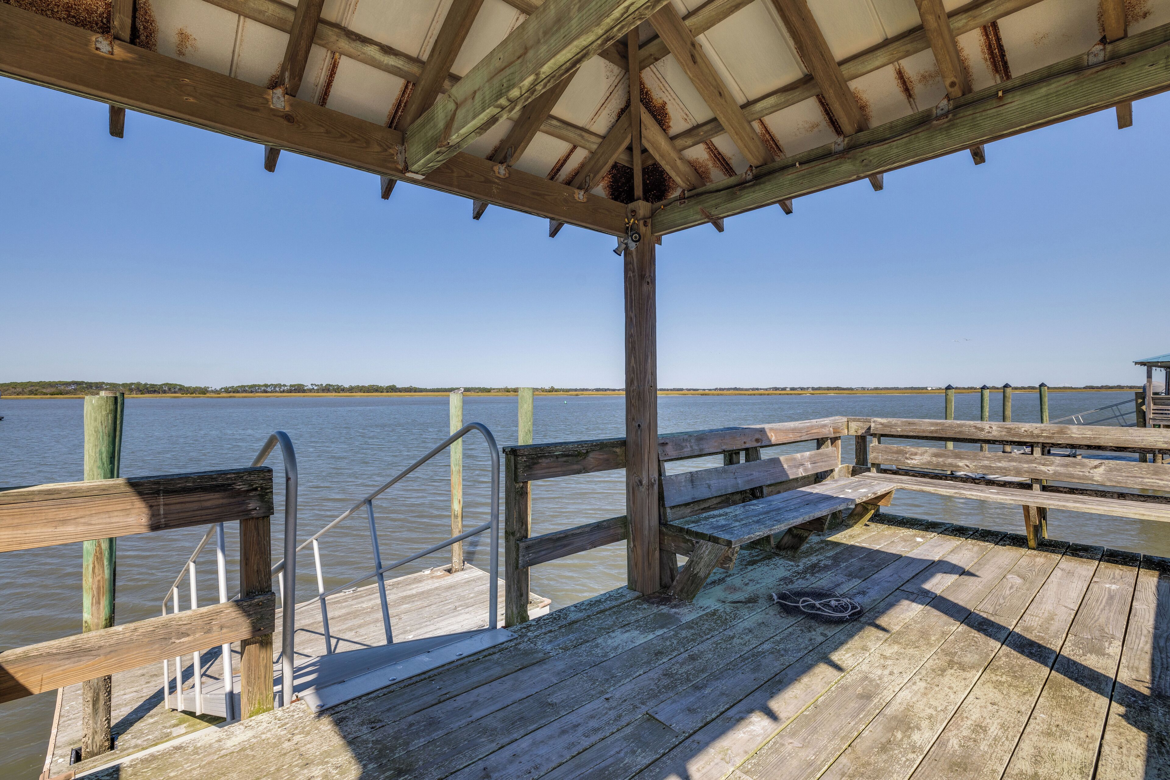 A wooden pier with benches and a metal railing, overlooking a calm body of water.