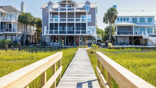 Una pasarela de madera que conduce a un edificio frente al mar con varios pisos, balcones y un porche cubierto.