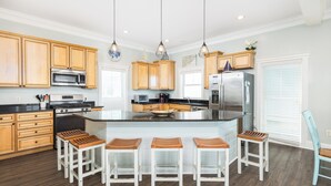 Una cocina moderna con armarios de madera, una isla central con taburetes, electrodomésticos de acero inoxidable e iluminación colgante.