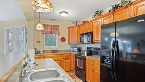 A kitchen with wooden cabinets, stainless steel appliances, a double sink, and a decorative pendant light. - Wintergreens R1112- Mtn Condo/View, Gated Resort, Indoor/Outdoor Pools & Hot Tub (Banner Elk)
